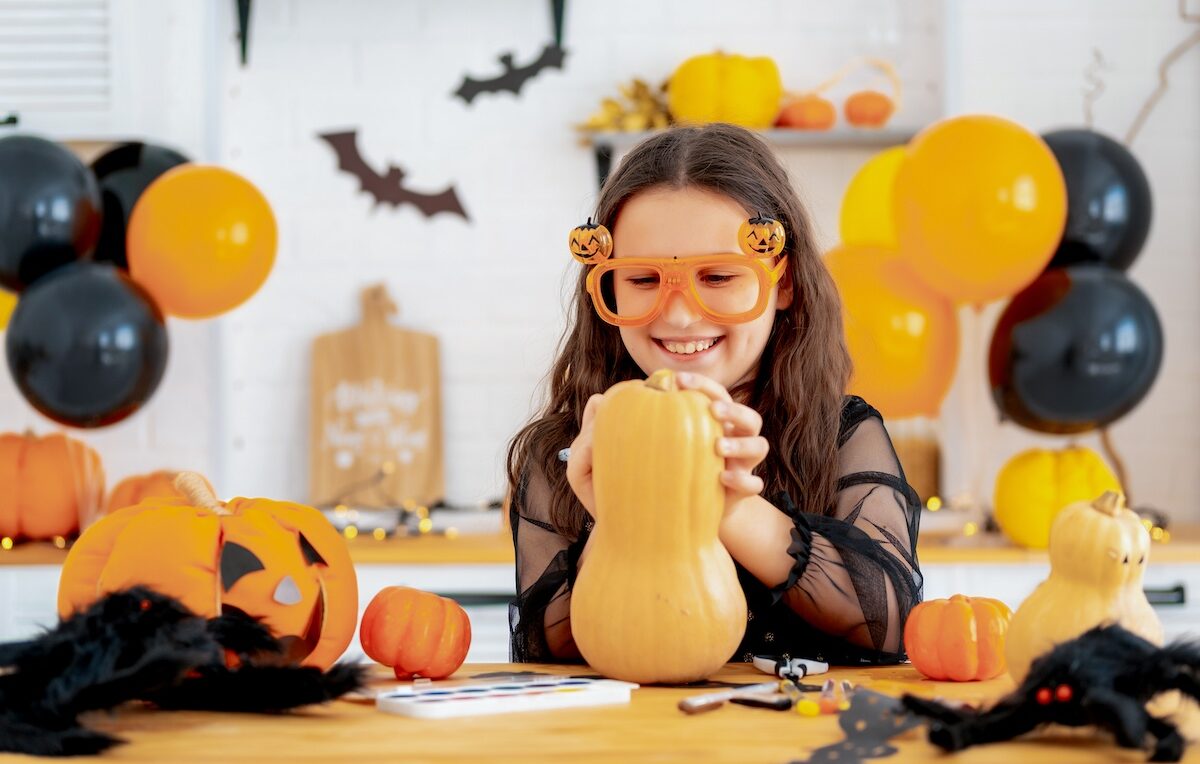 Halloween, a child in a witch costume is preparing for the Halloween holiday by coloring pumpkins at home in the kitchen with festive props, happy Halloween, blog