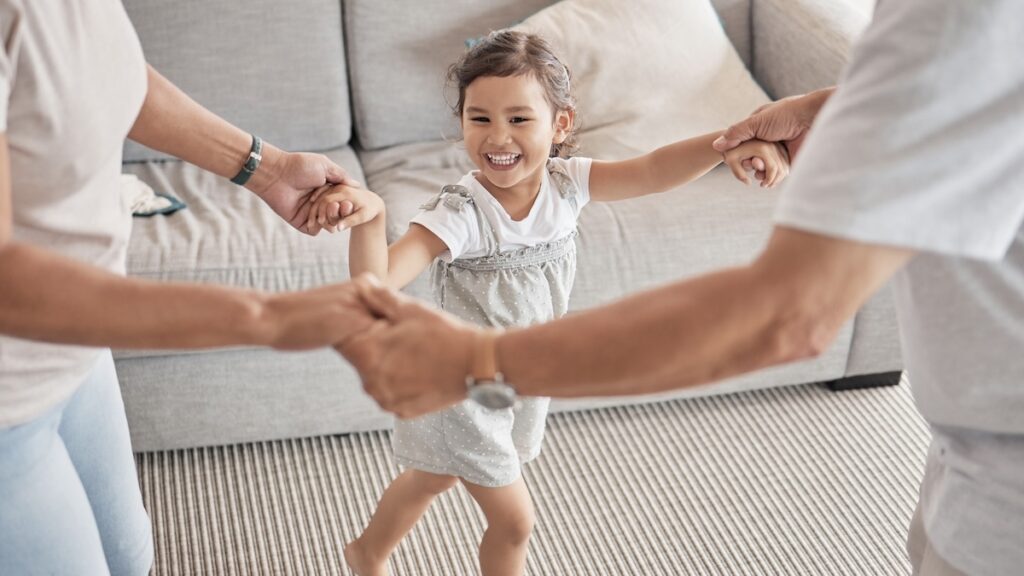 Happy family having a a dance party with a child, playing circle game while bonding, fun and holding hands with energy, happiness and joy with energetic asian girl. Kid, play and support with man and woman doing dance at home.