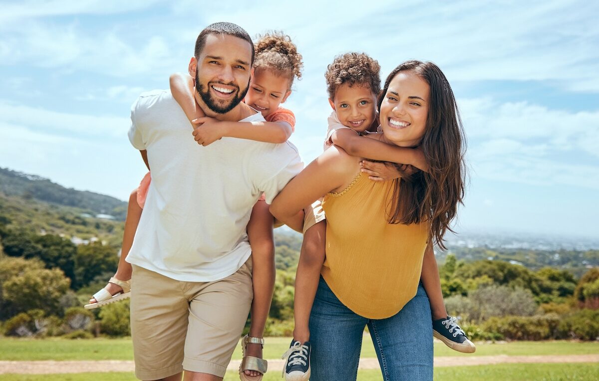 Active kids, happy family. Mom, dad and children on piggyback ride from parents in nature park for fun, summer time bonding and outdoor family activity. Black father, mother and kids smile together while playing on grass.