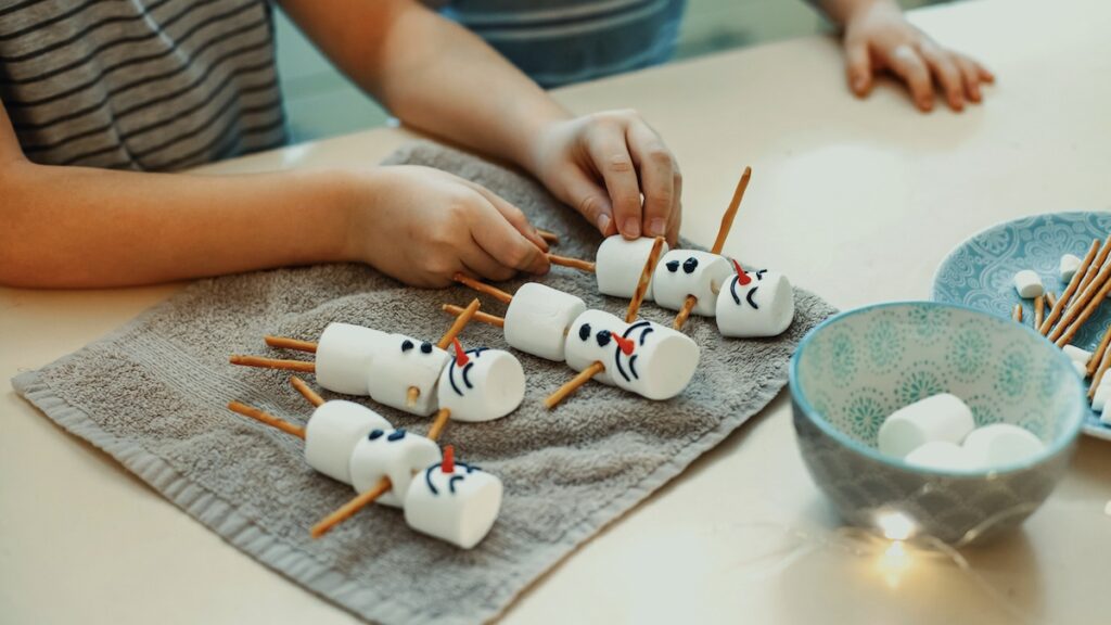 Two brothers make snowmen with marshmallows and pretzel sticks