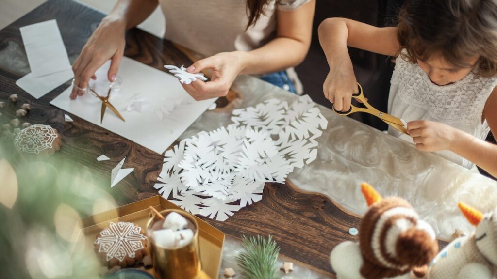 Mom and daughter cut snowflakes from white paper