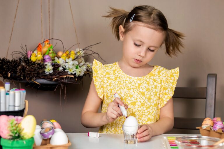 Fun and Creative Easter Activities for Kids, Little adorable girl in yellow dress painting Easter eggs with paintbrush