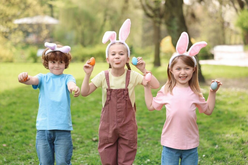 three children wearing easter bunny ears and holding up colorful easter egg, making happy memories